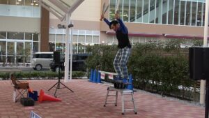 ローラーバランスの上でナイフのジャグリングに挑戦する大道芸人丸ちぇろ。滋賀県守山市のフレンドタウン守山(平和堂)の屋外イベント広場にて大道芸パフォーマンスをさせていただきました。